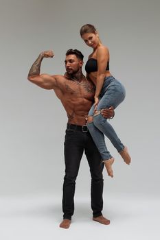 Muscular tattooed man embracing slim topless woman in panties on gray background