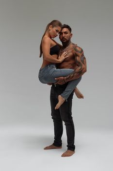 Muscular tattooed man embracing slim topless woman in panties on gray background