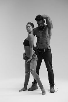 Black and white side view of topless woman and shirtless man looking at camera against gray background