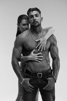 Black and white side view of topless woman and shirtless man looking at camera against gray background