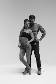 Black and white side view of topless woman and shirtless man looking at camera against gray background