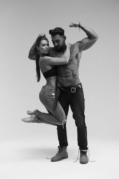 Black and white side view of topless woman and shirtless man looking at camera against gray background