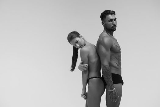 Black and white tattooed shirtless man and seductive topless woman looking away