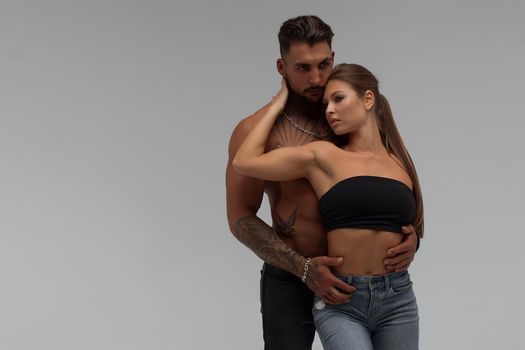 Muscular tattooed man embracing slim topless woman in panties on gray background