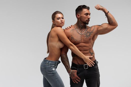 Muscular tattooed man embracing slim topless woman in panties on gray background