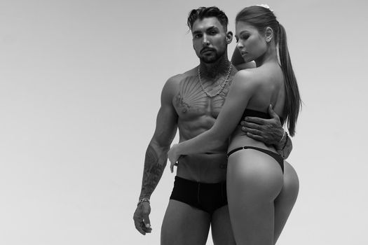 Black and white tattooed shirtless man and seductive topless woman looking away