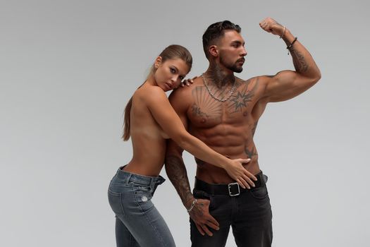 Muscular tattooed man embracing slim topless woman in panties on gray background