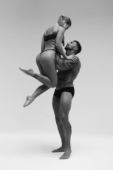 Black and white side view of topless woman and shirtless man looking at camera against gray background