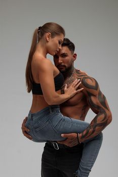 Muscular tattooed man embracing slim topless woman in panties on gray background