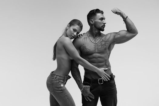 Black and white tattooed shirtless man and seductive topless woman looking away