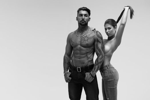 Black and white tattooed shirtless man and seductive topless woman looking away