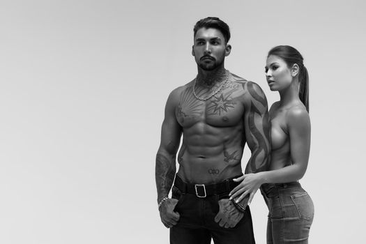 Black and white tattooed shirtless man and seductive topless woman looking away