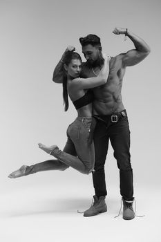 Black and white side view of topless woman and shirtless man looking at camera against gray background