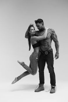 Black and white side view of topless woman and shirtless man looking at camera against gray background