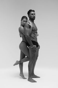 Black and white side view of topless woman and shirtless man looking at camera against gray background