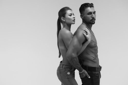 Black and white tattooed shirtless man and seductive topless woman looking away