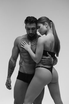 Black and white side view of topless woman and shirtless man looking at camera against gray background