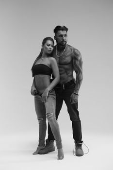 Black and white side view of topless woman and shirtless man looking at camera against gray background