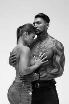 Black and white side view of topless woman and shirtless man looking at camera against gray background