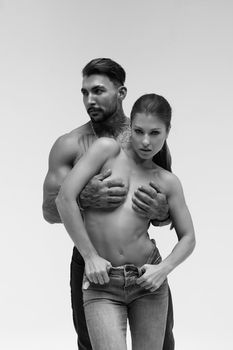 Black and white side view of topless woman and shirtless man looking at camera against gray background