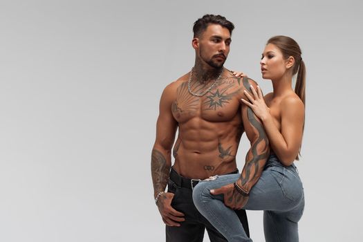 Muscular tattooed man embracing slim topless woman in panties on gray background