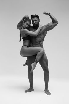 Black and white side view of topless woman and shirtless man looking at camera against gray background