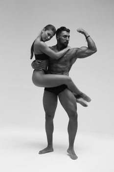 Black and white side view of topless woman and shirtless man looking at camera against gray background