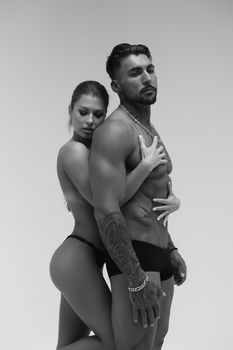 Black and white side view of topless woman and shirtless man looking at camera against gray background