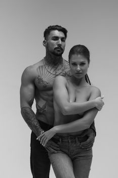 Black and white side view of topless woman and shirtless man looking at camera against gray background