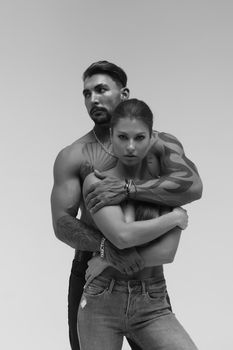 Black and white side view of topless woman and shirtless man looking at camera against gray background