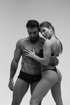 Black and white side view of topless woman and shirtless man looking at camera against gray background