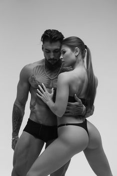 Black and white side view of topless woman and shirtless man looking at camera against gray background