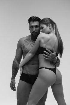 Black and white side view of topless woman and shirtless man looking at camera against gray background