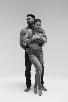 Black and white side view of topless woman and shirtless man looking at camera against gray background