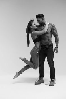 Black and white side view of topless woman and shirtless man looking at camera against gray background