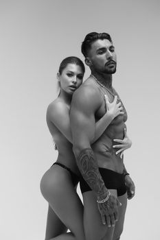 Black and white side view of topless woman and shirtless man looking at camera against gray background