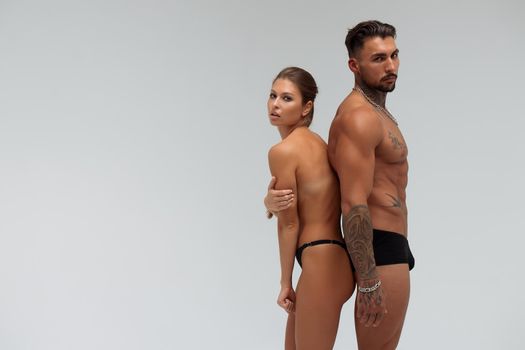 Muscular tattooed man embracing slim topless woman in panties on gray background