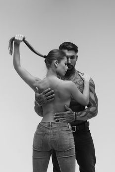 Black and white side view of topless woman and shirtless man looking at camera against gray background