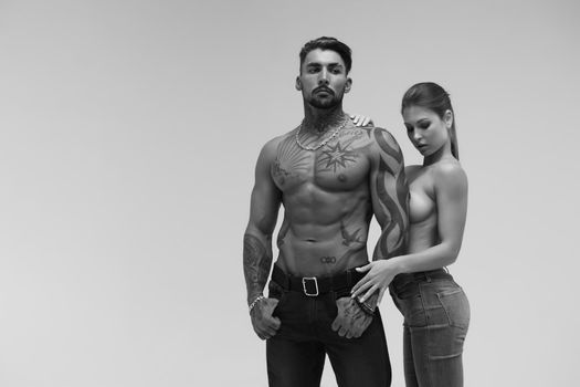 Black and white tattooed shirtless man and seductive topless woman looking away