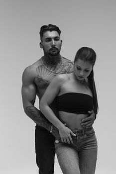 Black and white side view of topless woman and shirtless man looking at camera against gray background