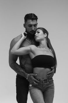 Black and white side view of topless woman and shirtless man looking at camera against gray background