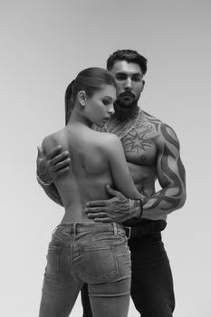 Black and white side view of topless woman and shirtless man looking at camera against gray background