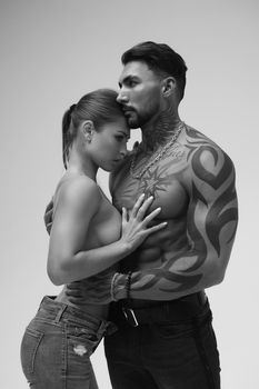 Black and white side view of topless woman and shirtless man looking at camera against gray background