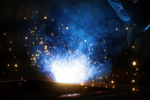 Welder at work. Welding of metal sparks and smoke in the workshop. Industrial Welder With gas Torch in Protective Helmet, welding metal profiles. The welding operation at construction site.