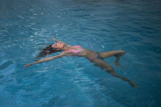 From above seductive woman touching wet hair and net while resting in clean pool water on resort