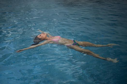 From above seductive woman touching wet hair and net while resting in clean pool water on resort