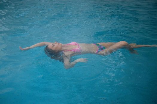 From above seductive woman touching wet hair and net while resting in clean pool water on resort