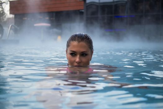 Seductive woman in pink bra crossing arms and looking away while resting in clean water of hot spring on resort