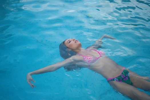 From above seductive woman touching wet hair and net while resting in clean pool water on resort