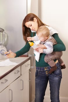 Young mom trying to multi-task while holding her baby son and his bottle.